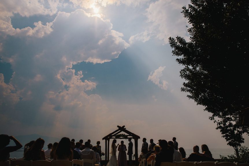 Sun rays shine through clouds as a wedding ceremony is pictured in silhouette.